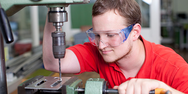 Ein junger Mann steht an einer Industriebohrmaschine.
