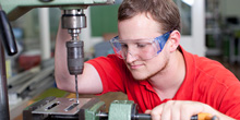 Ein junger Mann steht an einer Industriebohrmaschine