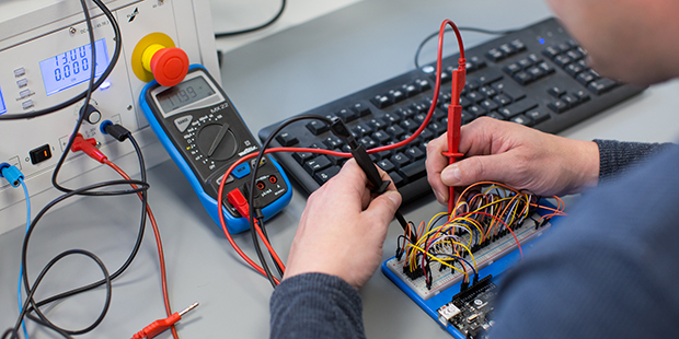 Ein farbiger Mann sitzt in einem Technikraum vor einem PC.