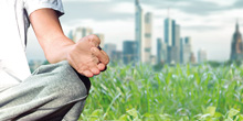 Eine Person meditiert auf einer Wiese vor der Skyline von Frankfurt am Main.