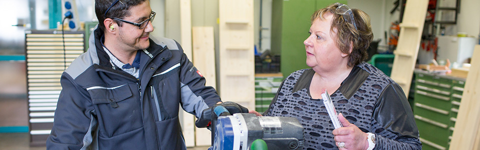 Ein Mann und eine Frau stehen an einem Arbeitsgerät in einer Werkstatt