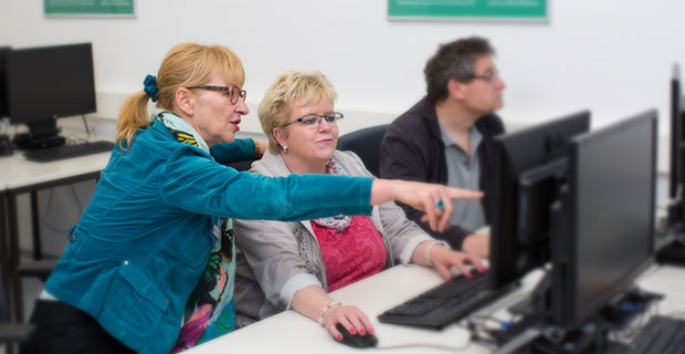 Eine Ausbilderin erklärt einer Frau etwas am PC.