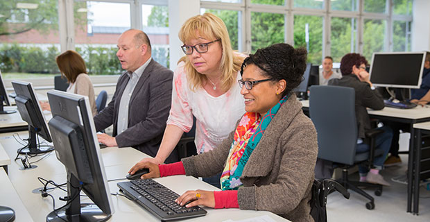 Eine Frau erklärt einer Frau mit Migrationshintergrund etwas in einem Computerraum.