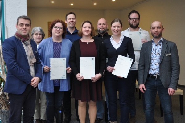 Einem besonderen Anlass gekleidete Personengruppe verschiedenen Alters schaut in die Kamera. Drei Personen halten ein Zertifikat in der Hand.