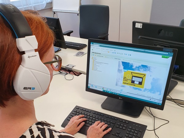 Eine Frau sitzt Kopfhörer tragend an einem Schreibtisch und schaut auf einen Monitor, der die Oberfläche von SAP anzeigt.