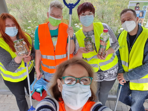 Fünf Personen mit Warnwesen halten mit Zigarettenresten gefüllte Gläser und Greifzangen in der Hand und schauen in die Kamera. 
