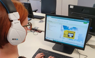 Eine Frau sitzt Kopfhörer tragend an einem Schreibtisch und schaut auf einen Monitor, der die Oberfläche von SAP anzeigt.