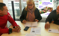 Drei Personen sitzen an einem Tisch, auf dem verschiedene Ausdrucke liegen und unterhalten sich.