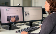 Eine Frau sitzt an einem Schreibtisch und schaut auf einen PC, der die Website des BFW Frankfurt zeigt.